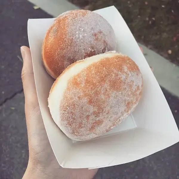 A hand holding two malasada doughnuts.
